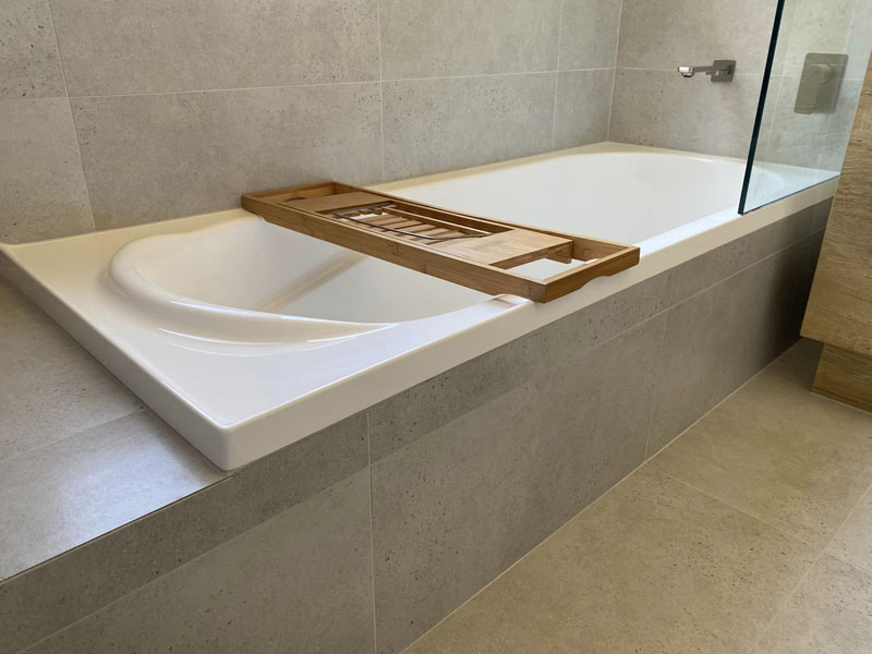 Tiled bath surround with timber bath caddy and glass shower screen