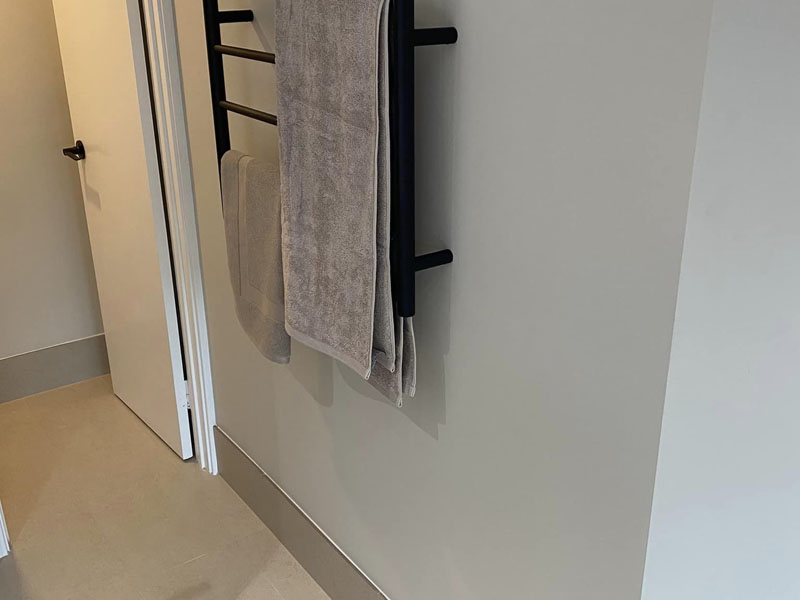 Black heated towel rail with grey towels beside a doorway
