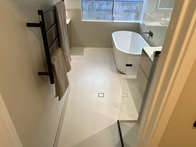 Bathroom with freestanding bath, black towel rail and pale floor tiles
