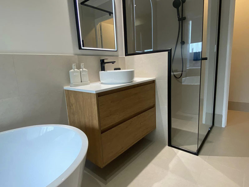 Freestanding bath beside a timber-look vanity and black-framed shower