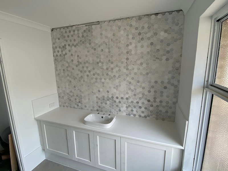 White built-in cabinetry and basin below a grey hexagon mosaic feature wall
