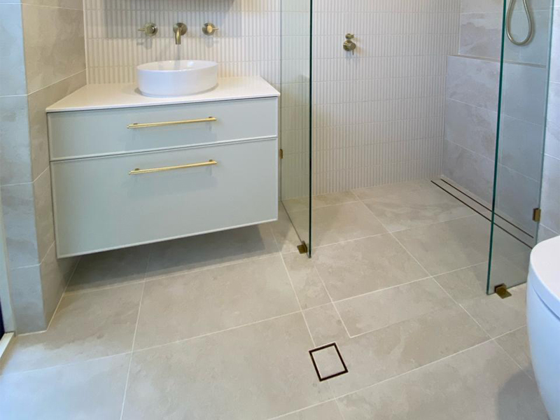Wall-hung vanity with brass handles and round basin beside a walk-in shower