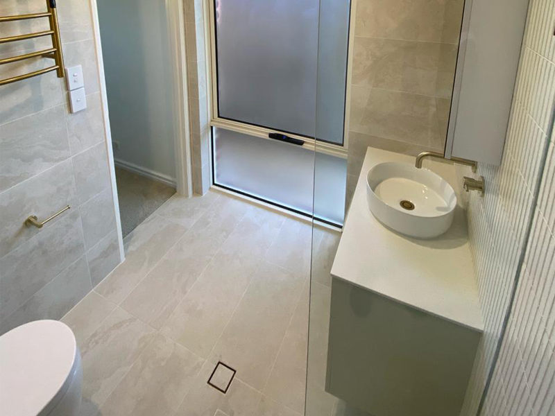 Round basin on a white vanity with brass tapware beside a frosted window