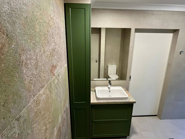 Bathroom with green vanity and tall cabinet beside a patterned feature wall