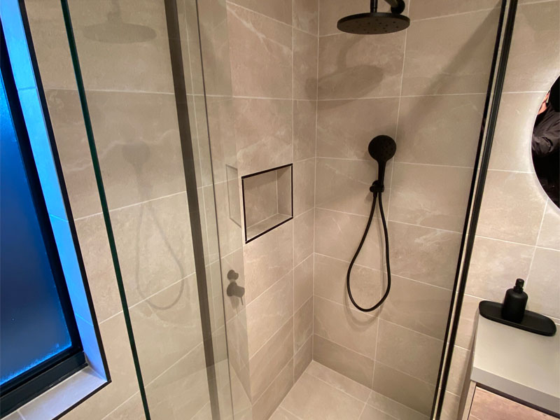 Tiled shower with black rain shower head, hand shower and wall niche