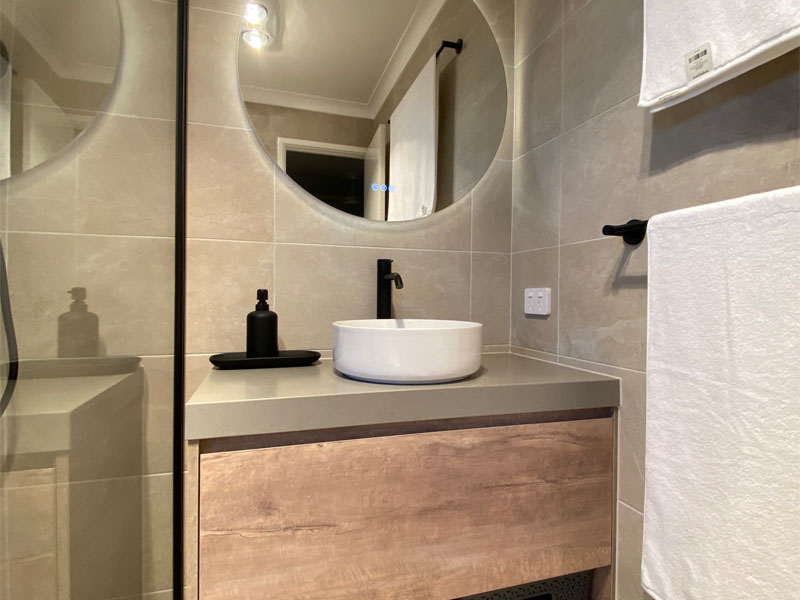 Bathroom with round backlit mirror, timber-look vanity and white vessel basin